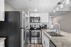 A modern kitchen with stainless steel appliances, a granite countertop, and white cabinetry. - Gulf-Front Condo | Beach Chairs, Balcony & 3 Pools (Panama City Beach)