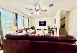 A living room with a leather sofa, a ceiling fan, a TV displaying 'NETFLIX,' and a staircase. - Lux Mins To Cowboys AT&T Stadium, Six Flags, TX Rangers, TX Live (Arlington)