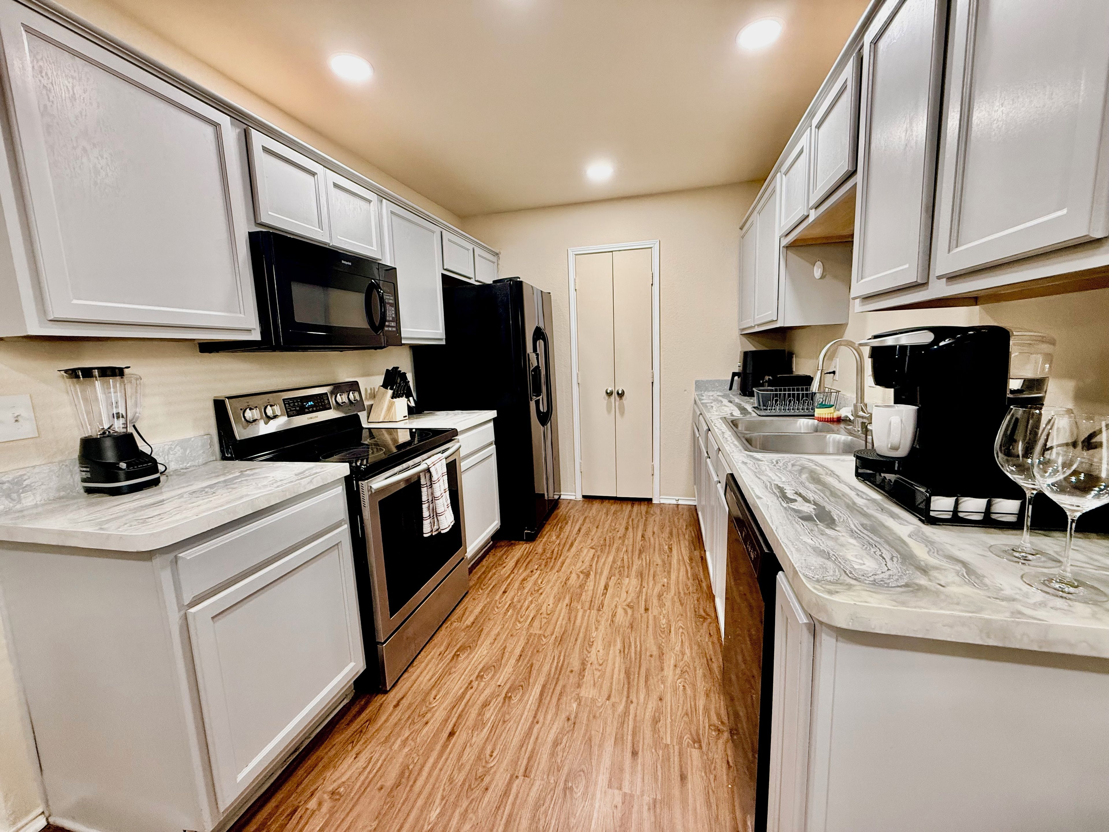 A kitchen with white cabinets, a black microwave, a black refrigerator, a stove, a dishwasher, and a marble countertop.