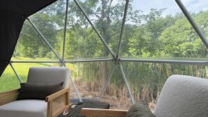 Une tente offrant une vue sur un champ verdoyant et des arbres. À l’intérieur, on trouve deux chaises avec des coussins.