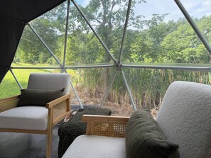 Tienda de campaña con vista a un campo cubierto de césped y árboles. En el interior, hay dos sillones con cojines.