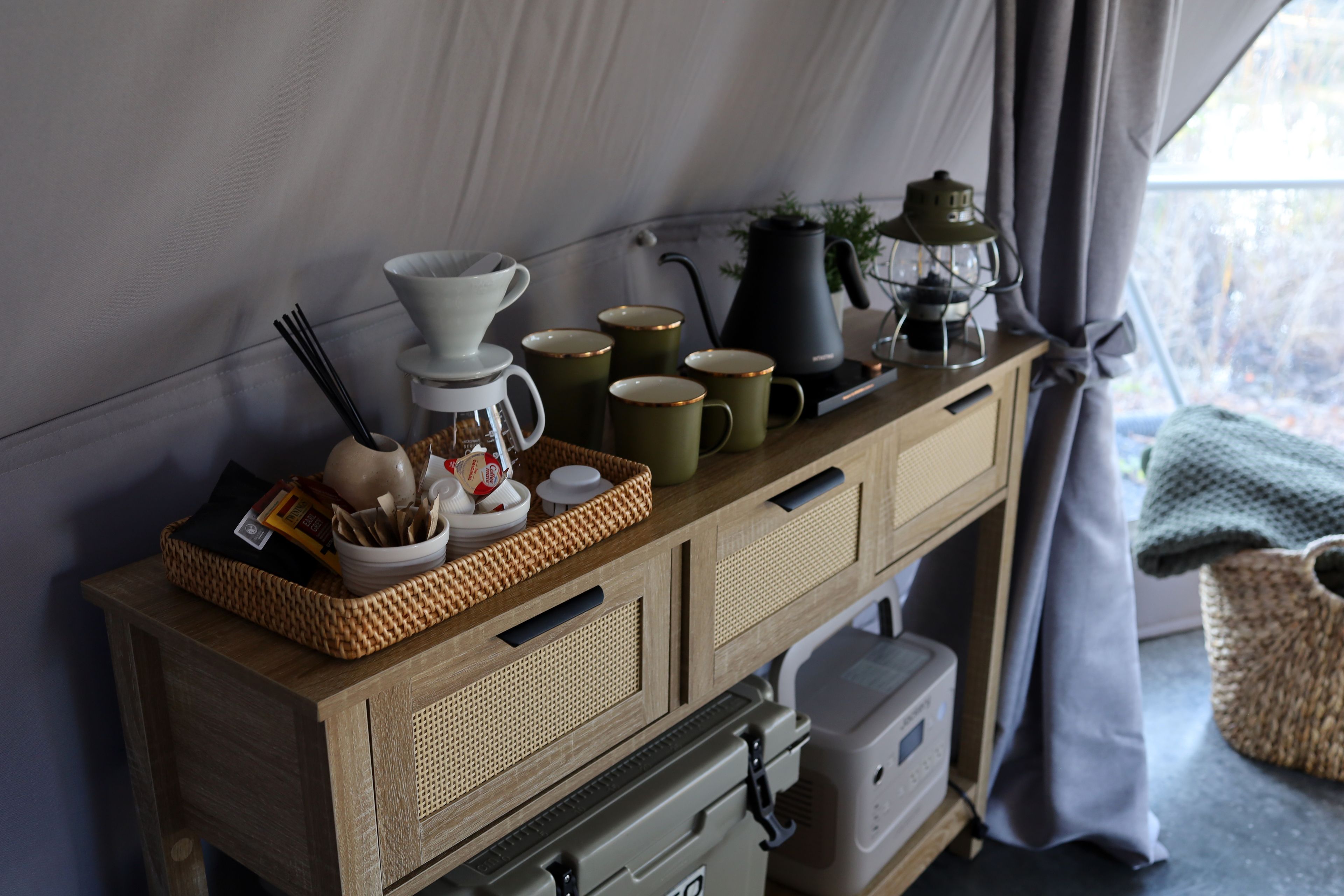 A wooden cabinet with storage drawers, a coffee maker, and a tea kettle on top.