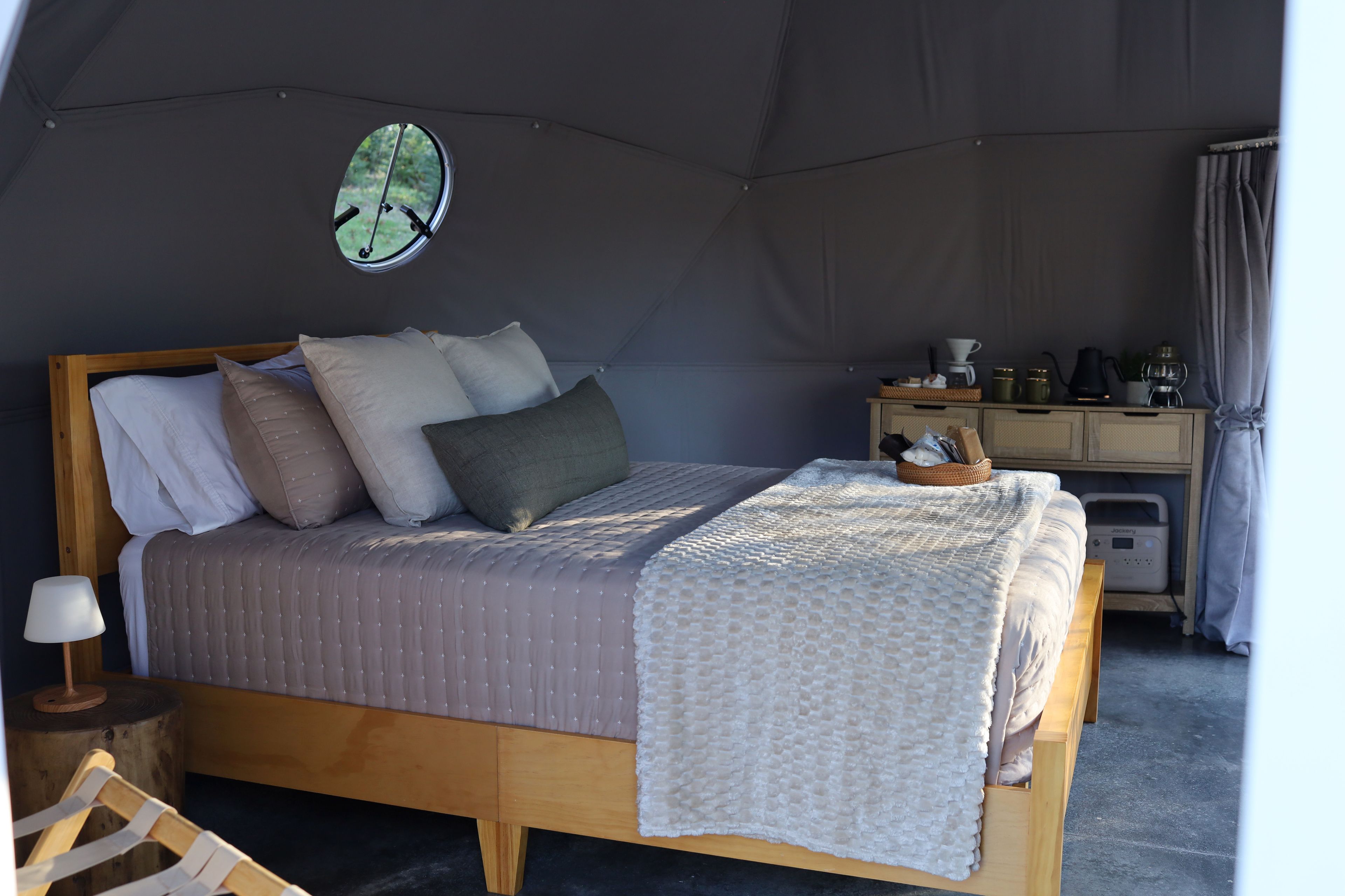 Una habitación con tienda de campaña, una cama, un escritorio pequeño y una ventana con vista a la vegetación.