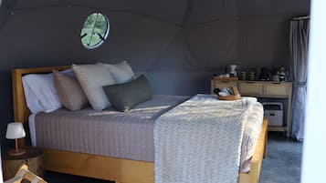 Una habitación con tienda de campaña, una cama, un escritorio pequeño y una ventana con vista a la vegetación.