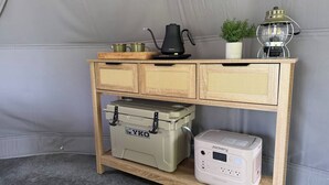 Une console en bois sur laquelle sont posés un réfrigérateur portable de la marque Yoko, une bouilloire, un radiateur d’appoint et une petite plante en pot.