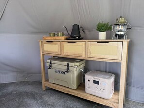 Una consola de madera con un enfriador Yoko, una tetera, un calentador portátil y una pequeña planta en maceta.