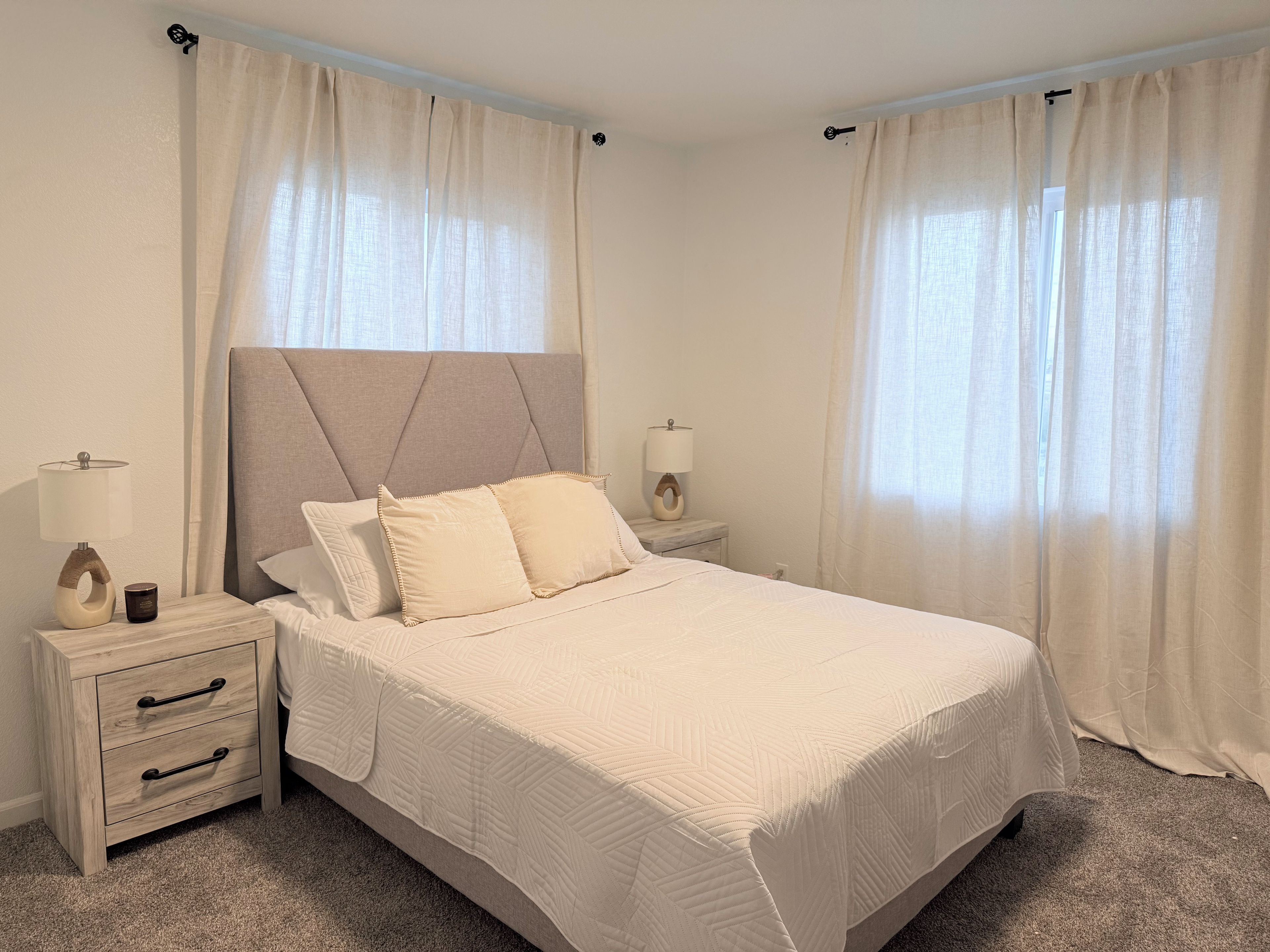 A bedroom with a bed, two bedside tables, a nightstand, and curtains.