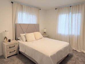 A bedroom with a bed, two bedside tables, a nightstand, and curtains.