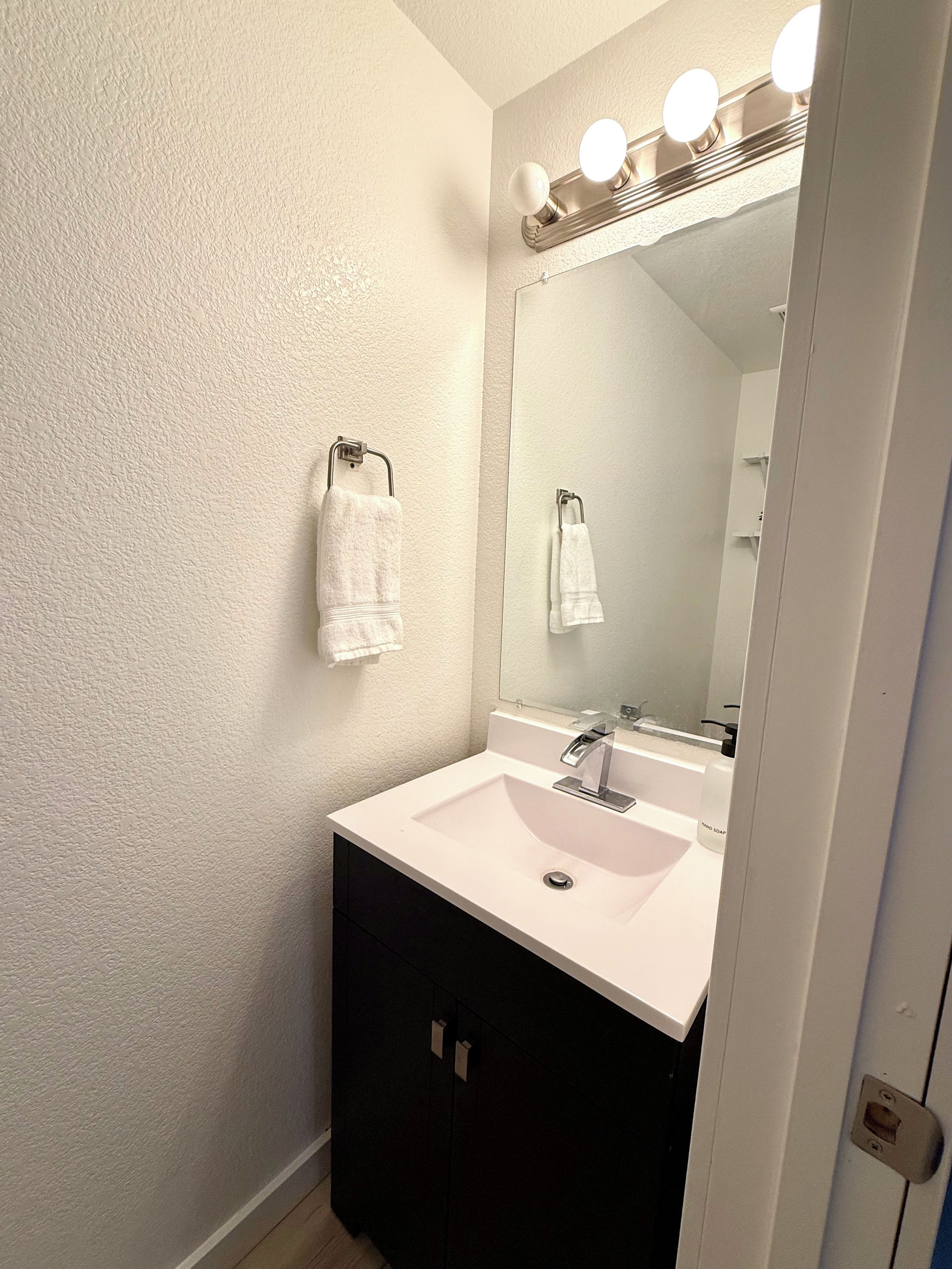 A bathroom with a white sink, a mirror with lights, and two towels hanging on hooks.