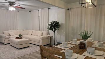 A modern living room with a sofa, ottoman, and a dining table set with white plates and bowls.