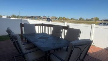 An outdoor patio with a table and chairs, a white fence, and a view of a road and buildings in the distance.