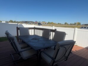 Un patio al aire libre con una mesa y sillas, una valla blanca y vistas a una carretera y edificios a lo lejos.