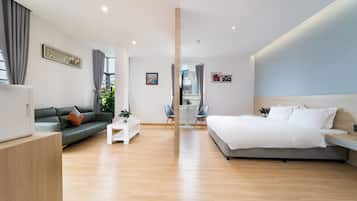 A modern hotel room with a bed, sofa, and a dining area with a table and chairs.