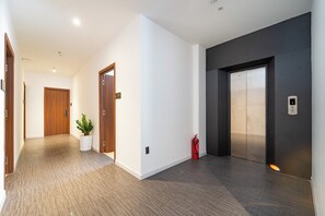 A hallway with a carpeted floor, a potted plant, a fire extinguisher, and an elevator.