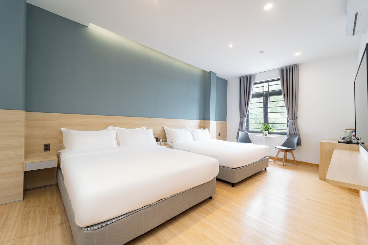 A hotel room with two beds, a desk, and a window with curtains.
