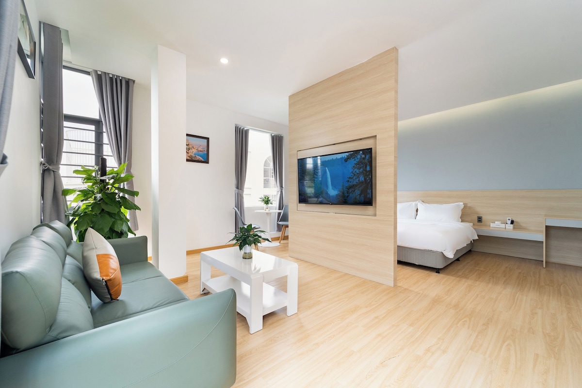 A modern hotel room with a sofa, a coffee table, a TV, and a bed.