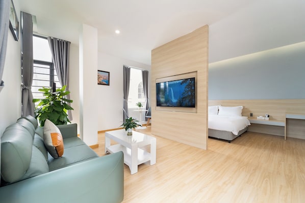 A modern hotel room with a sofa, a coffee table, a TV, and a bed.