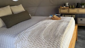 Una tenda con un letto, una finestra rotonda e un comodino con degli oggetti.