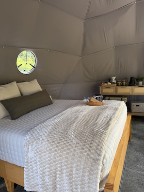 Una habitación con carpa, una cama, un ventanal redondo y una mesita de noche con objetos.