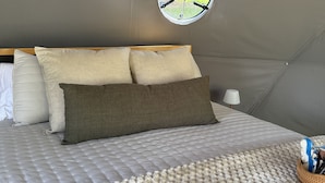 Una stanza con tende, un letto, cuscini, una finestra circolare e una lampada.