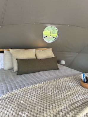 Una habitación con carpa, una cama, almohadas, un ventanal redondo y una lámpara.