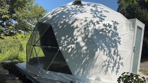 Una struttura a forma di cupola con un lato trasparente, circondata da rocce e vegetazione.