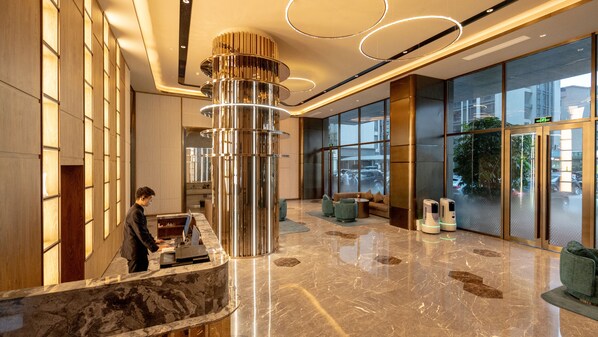 A modern lobby with a reception desk, a large cylindrical light fixture, and a seating area with sofas.
