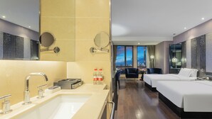 Ein Hotelzimmer mit großzügigem Badezimmer, zwei Betten, einem Schreibtisch und Blick auf die Stadtlandschaft.