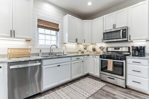 A modern kitchen with white cabinetry, stainless steel appliances, and a patterned rug. - 3-bedroom house minutes from Shenandoah - hot tub, kid-friendly and charming (Front Royal)