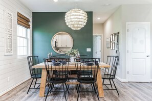 A dining room with a wooden table, black chairs, a hanging light fixture, and a green accent wall. - 3-bedroom house minutes from Shenandoah - hot tub, kid-friendly and charming (Front Royal)