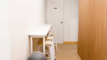 Un couloir étroit avec une porte blanche, une poubelle et une table blanche avec des chaises.