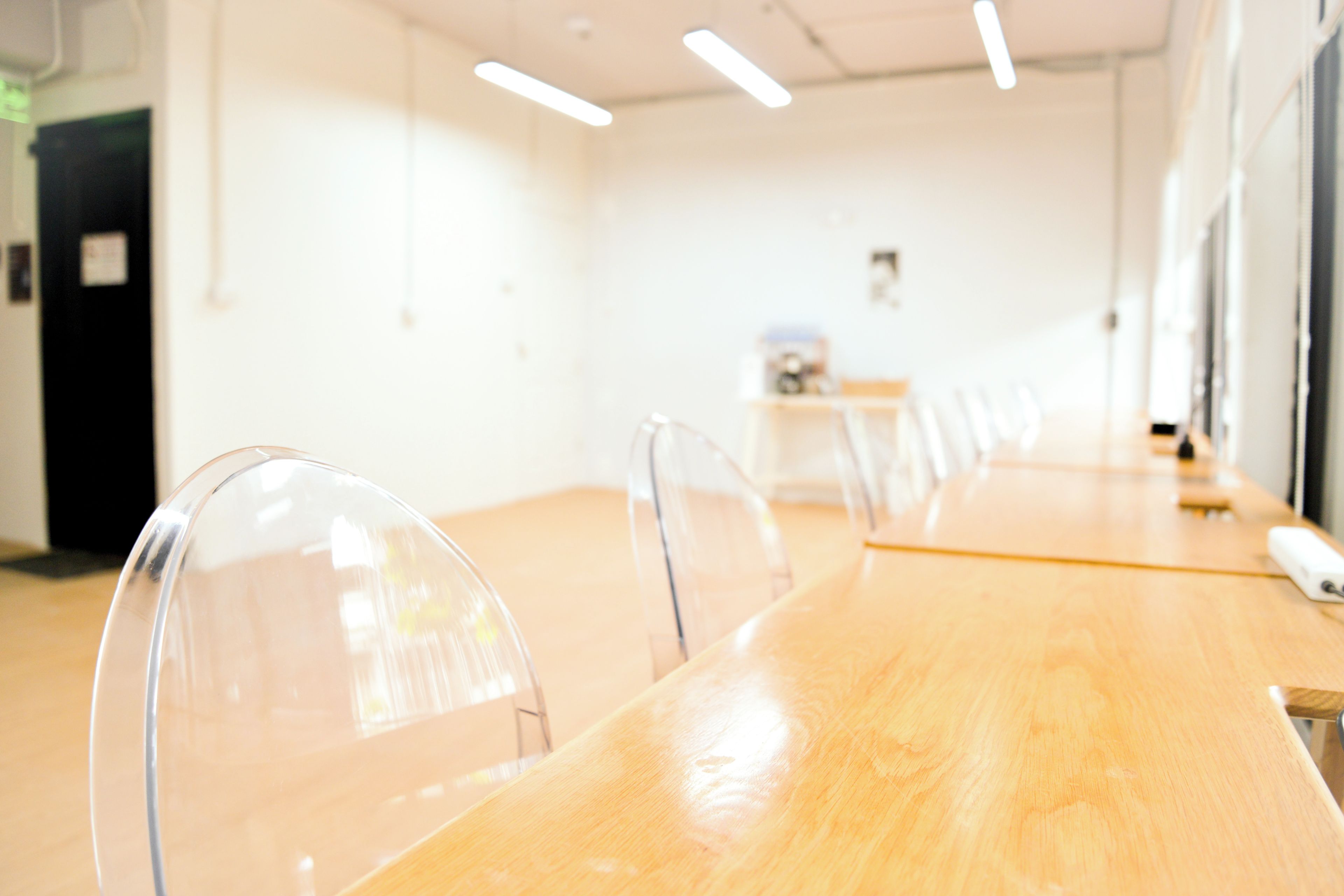 Un salón de conferencias con una larga mesa de madera, sillas de plástico transparente e iluminación colgante.
