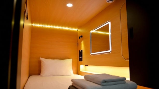 Una camera d'albergo con un letto, un comodino, una lampada a muro e uno specchio.