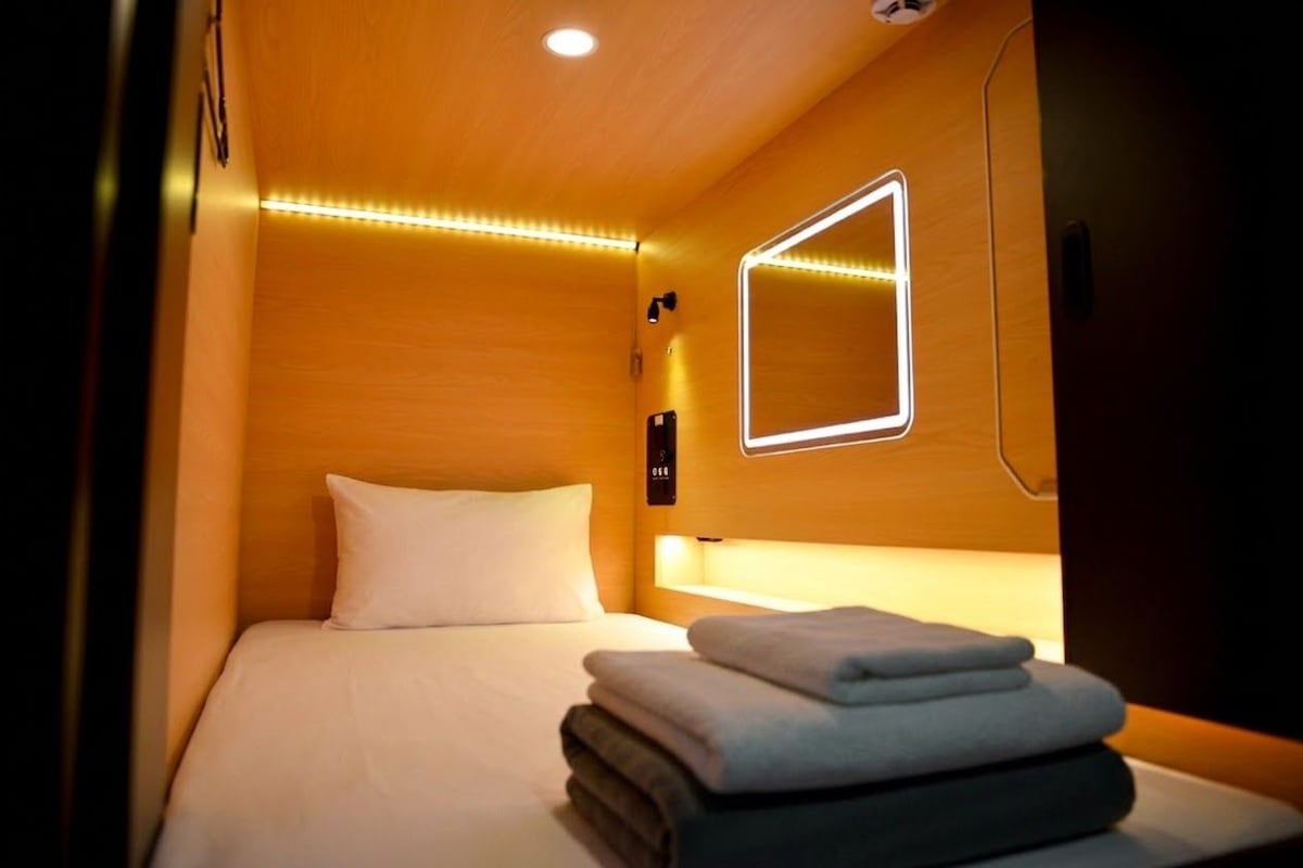 Una habitación de hotel con cama, mesita de noche, lámpara de pared y espejo.