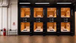 Una hilera de seis cabañas individuales con números del 01 al 08, cada una con una cama, un pequeño estante y una luz propia.