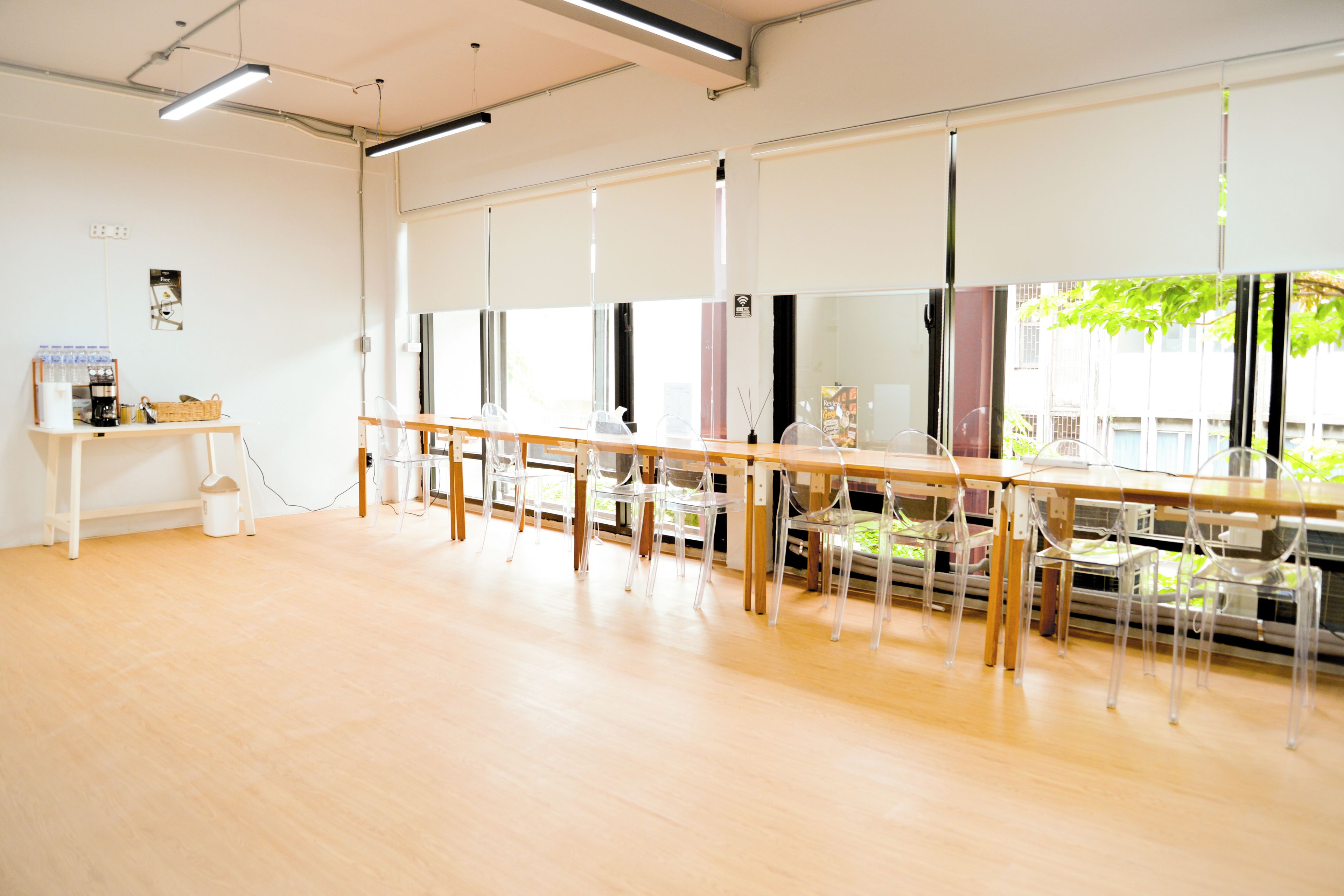 Una habitación amplia con una larga mesa de madera y sillas de plástico transparente, una pizarra y un ventanal con vistas a zonas verdes.
