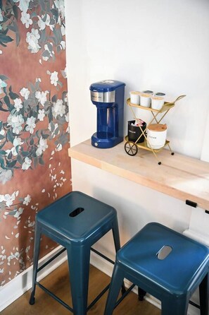 A room with a coffee maker on a shelf, a cart with containers, and two stools. - Charming Stay Near Historic District St. Augustine (St. Augustine)