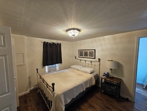 A bedroom with a single bed, a nightstand, a lamp, a window with a curtain, and a ceiling light fixture. - Bradleyville White House (Bradleyville)