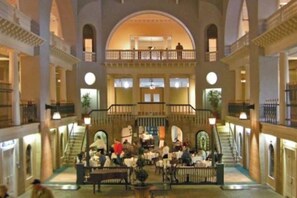 Ein mehrgeschossiges Atrium mit einer zentralen Treppe, verschiedenen Sitzbereichen und einem Balkon mit Blick auf den Innenraum.