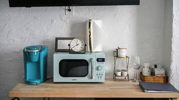 A kitchenette with a coffee maker, microwave, clock, and a small shelf with kitchenware.