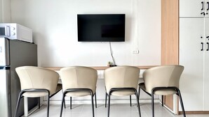 Una cucina moderna con una TV a schermo piatto montata a parete, un frigorifero e tre sedie attorno a un tavolo di legno.