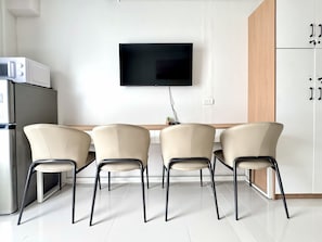 A modern kitchen with a flat-screen TV mounted on the wall, a refrigerator, and three chairs with a wooden table in front. - Royal Oceancrest Panglao 1 (Dauis)