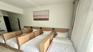 Una camera d'albergo con un letto grande, una testata imbottita con altoparlanti integrati, un quadro raffigurante una spiaggia e un bagno visibile attraverso una porta aperta.