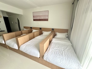 A hotel room with a large bed, a headboard with built-in speakers, a painting of a beach scene, and a bathroom visible through an open door. - Royal Oceancrest Panglao 1 (Dauis)