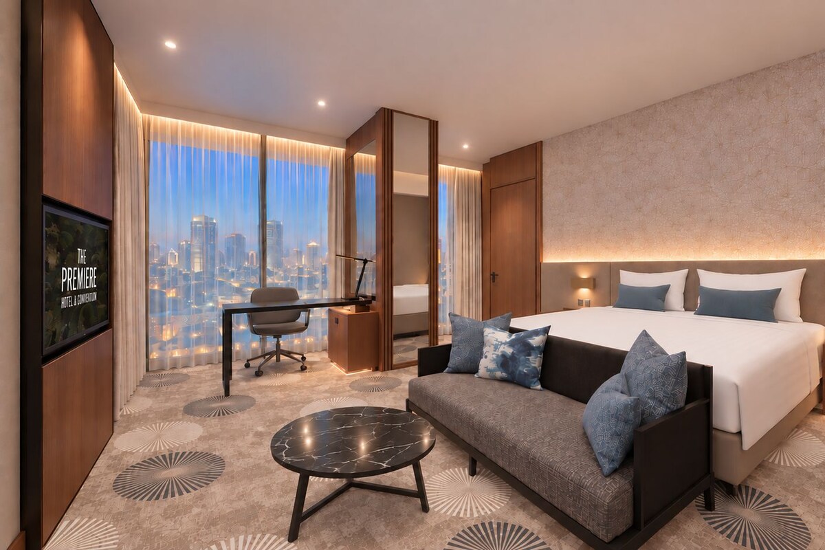 A modern hotel room with a large bed, a sofa, a desk, and a television.