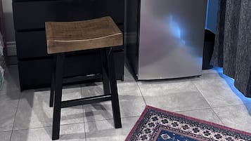 Een keuken met een zwart aanrecht, een roestvrijstalen koelkast, een houten kruk en een vloerkleed met een patroon.