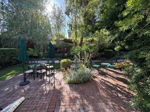 Eine Terrasse im Freien mit Backsteinfrauen, grünen Sonnenschirmen und einer Sitzgruppe mit Tischen und Stühlen.
