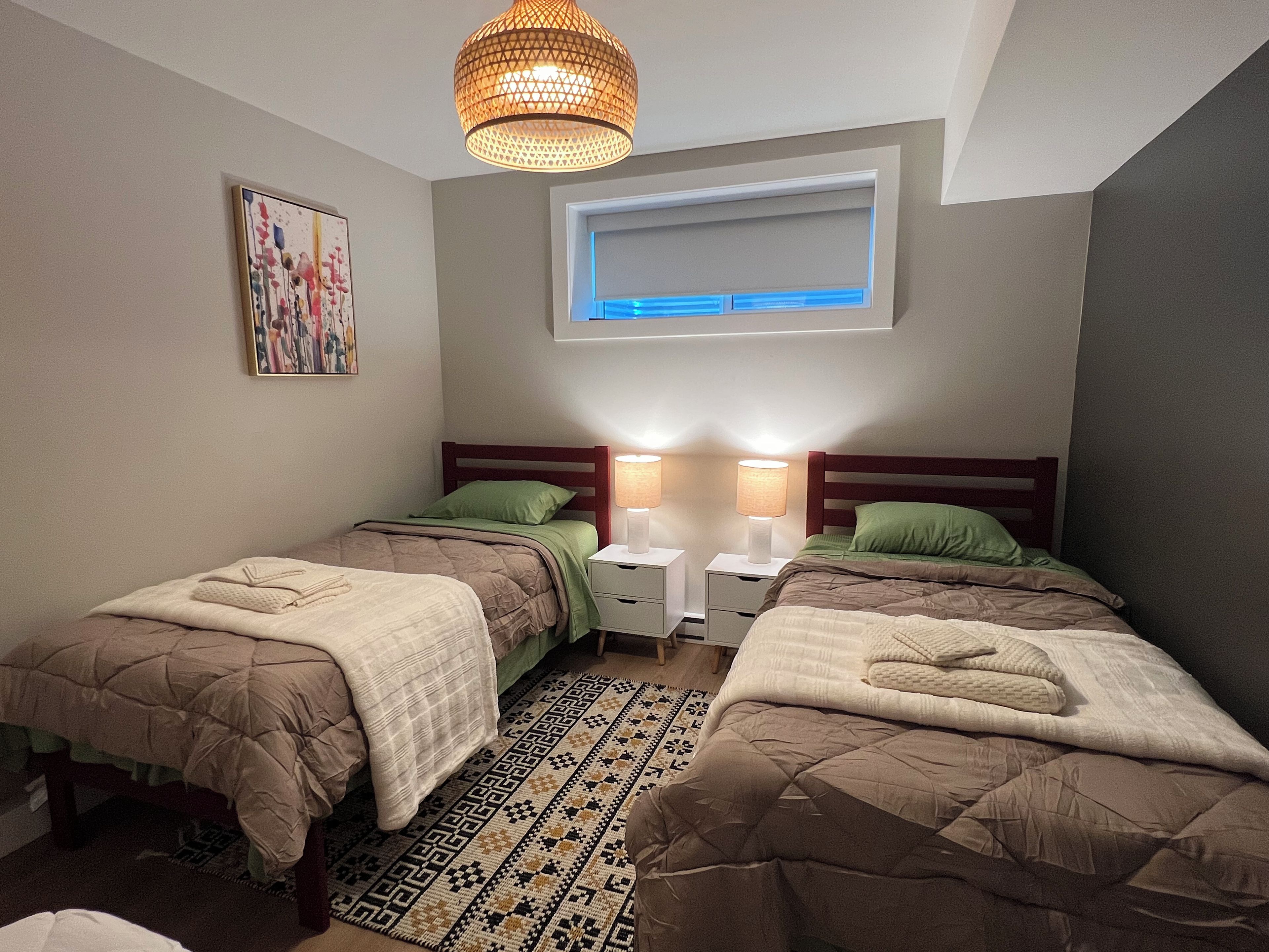 Ein Schlafzimmer mit zwei Betten, einem gemusterten Teppich, einer Deckenleuchte und einem Fenster.