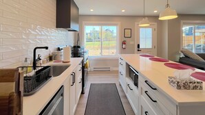 Une cuisine moderne avec des meubles blancs, un évier en acier inoxydable et un grand îlot central doté d’un four à micro-ondes.