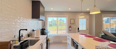 A modern kitchen with white cabinetry, a stainless steel sink, and a large island with a microwave.